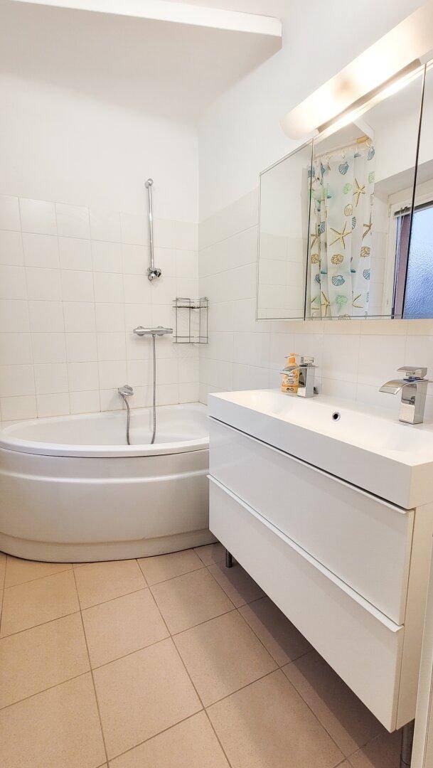 Badezimmer mit Eckbadewanne, modernem Waschtisch und hellen Fliesen, ausgestattet mit einem Spiegelschrank.