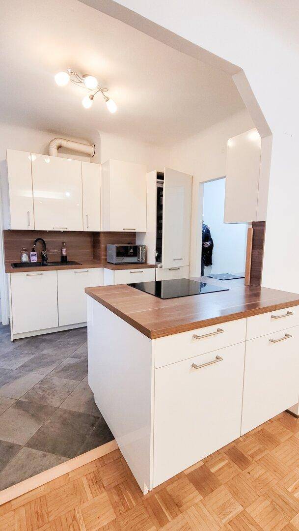 Moderne Einbauküche mit weißen Hochglanzschränken, Holz-Arbeitsplatten und integrierten Geräten.