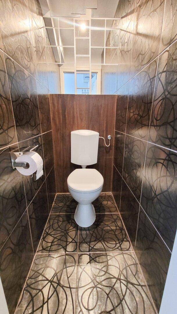 Modern gefliestes Gäste-WC mit Wand-WC und dekorativen Fliesen an Wänden und Boden.