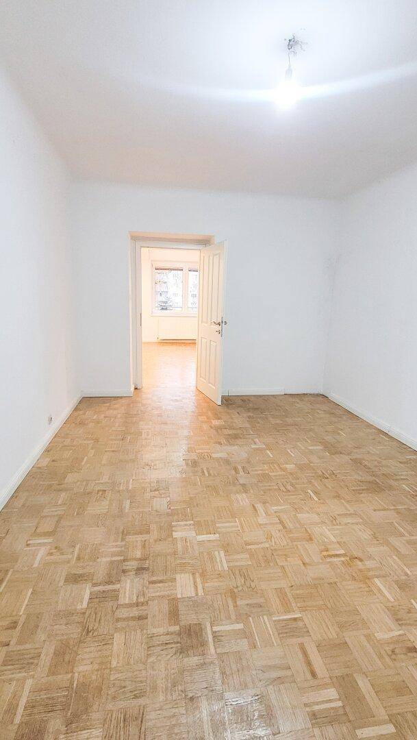 Helles Zimmer mit Parkettboden und Blick in den angrenzenden Raum, ideal als Schlaf- oder Arbeitszimmer.