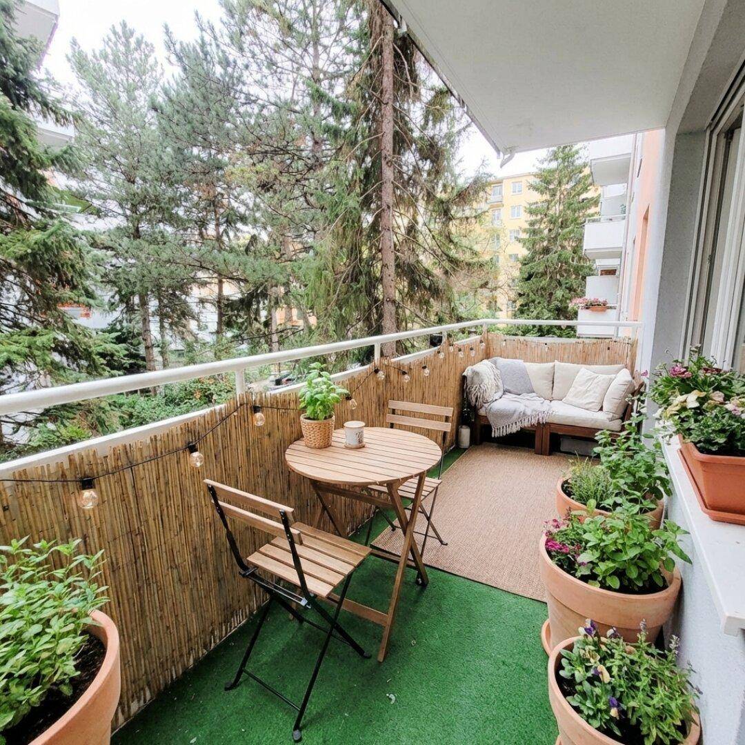 Gemütlicher Balkon mit Sitzgelegenheiten, Pflanzen und Blick auf hohe Bäume.