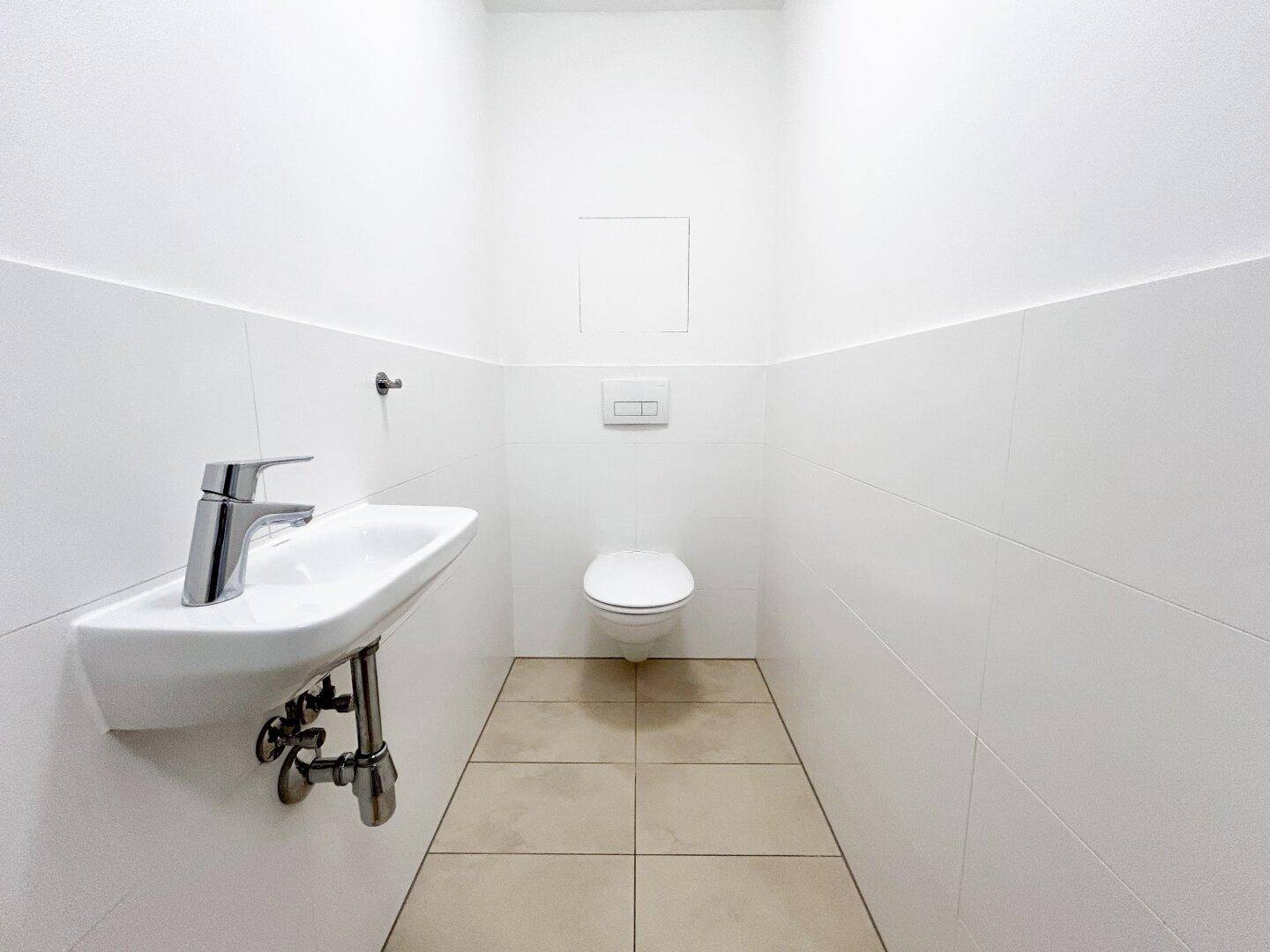 Separates Gäste-WC mit wandhängender Toilette und kleinem Waschbecken.