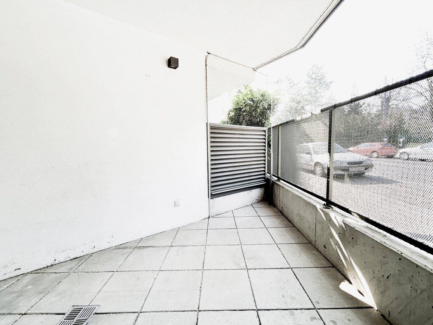 Gedeckte Terrasse mit Fliesenboden und Blick auf den Parkplatz.