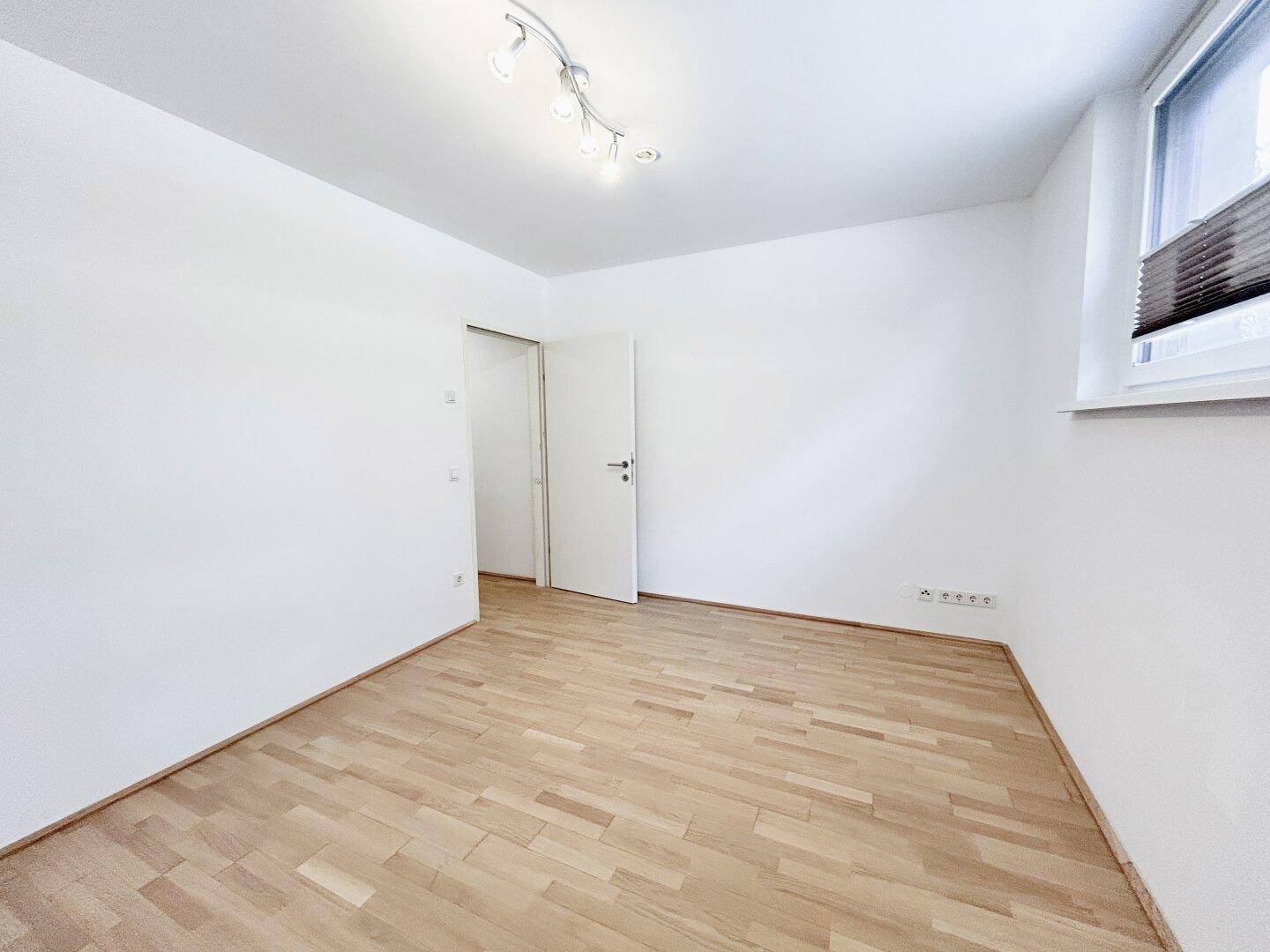 Leeres Zimmer mit Parkettboden, weiß gestrichenen Wänden und Fenster.