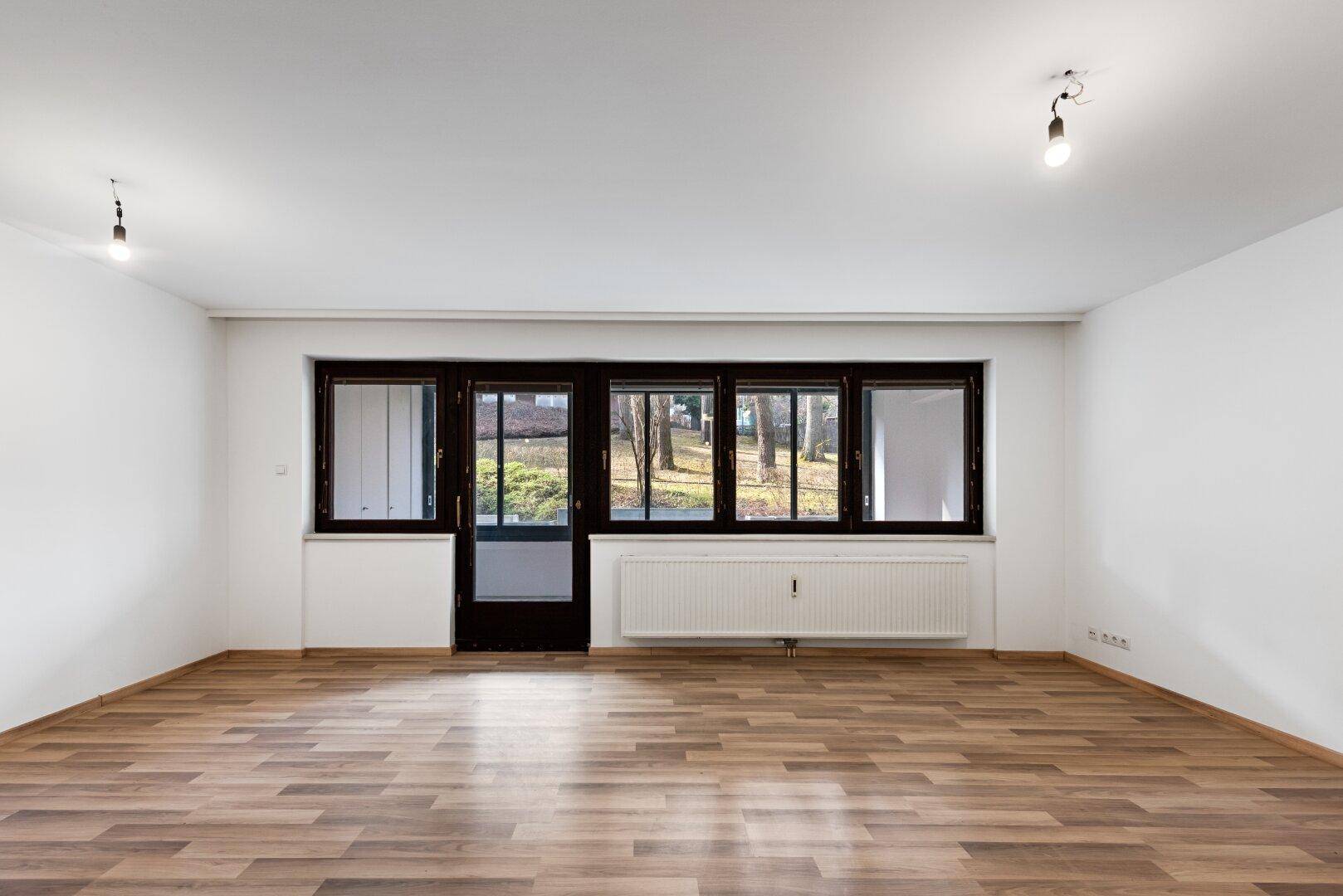 Heller Wohnbereich mit Laminatboden und breiter Fensterfront, die den Raum mit Licht füllt.