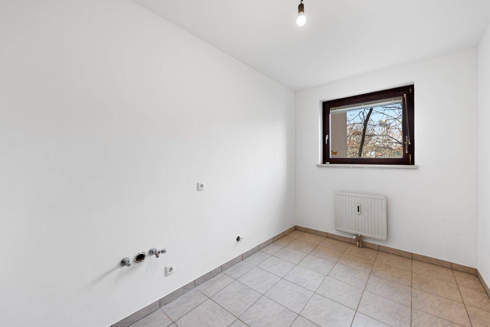 Leerer Küchenraum mit Fliesenboden und Anschlüssen für eine zukünftige Einbauküche.