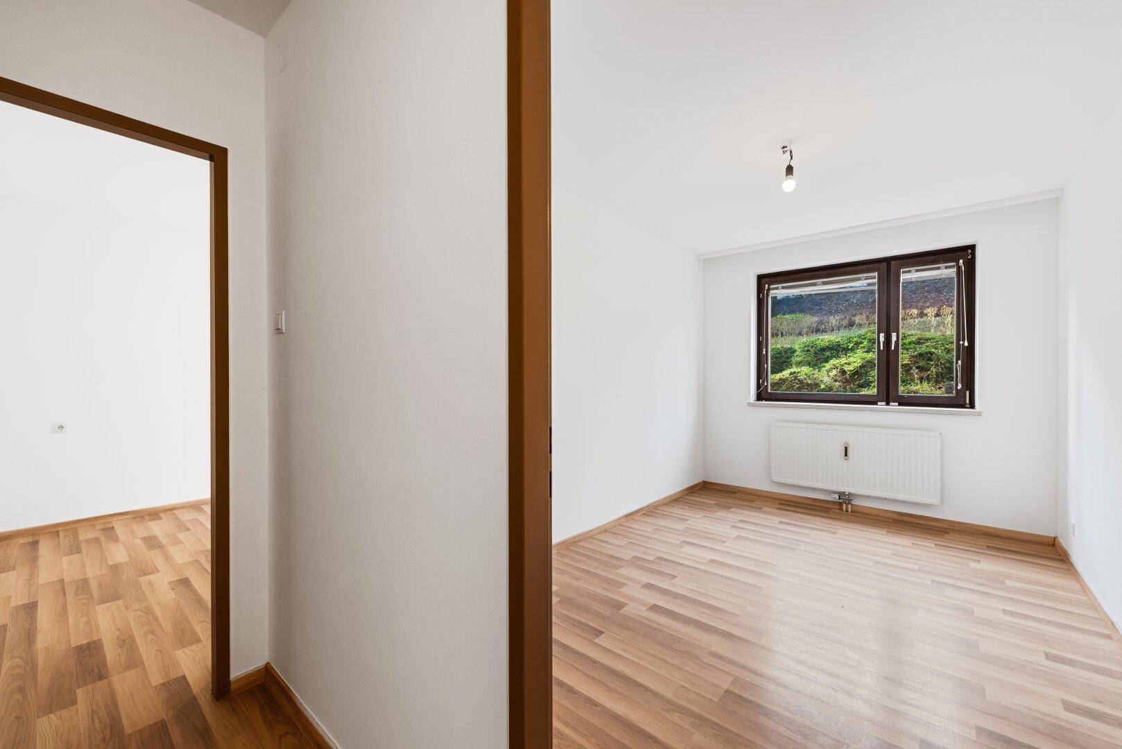 Helles Zimmer mit Laminatboden und Fenster mit Blick ins Grüne, ideal als Schlaf- oder Arbeitszimmer.