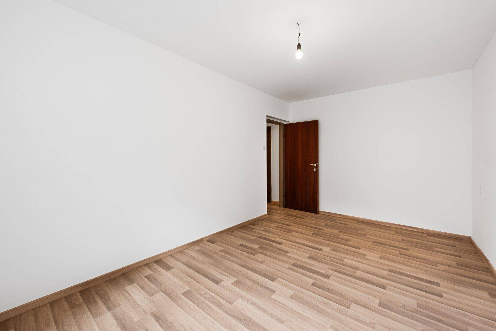 Helles Zimmer mit Laminatboden und einer Holztür, die zu einem weiteren Raum führt.