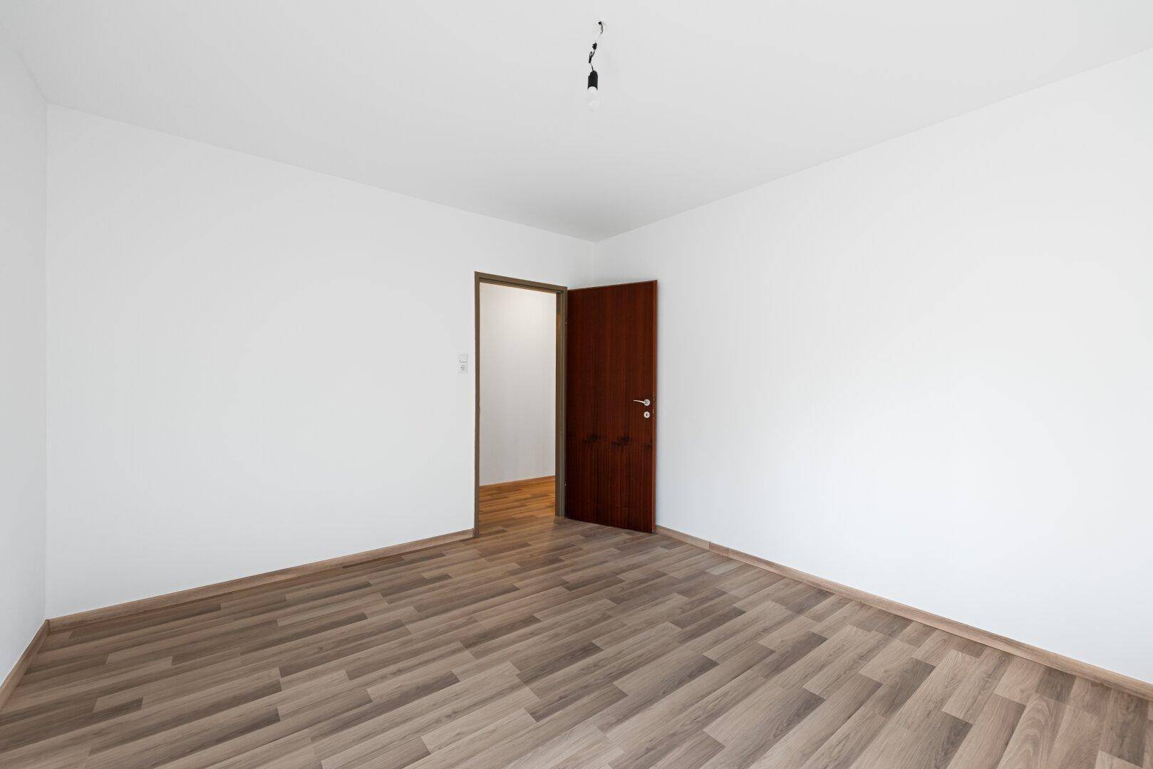Geräumiges Zimmer mit Laminatboden und offener Holztür, die den Blick in den angrenzenden Bereich freigibt.