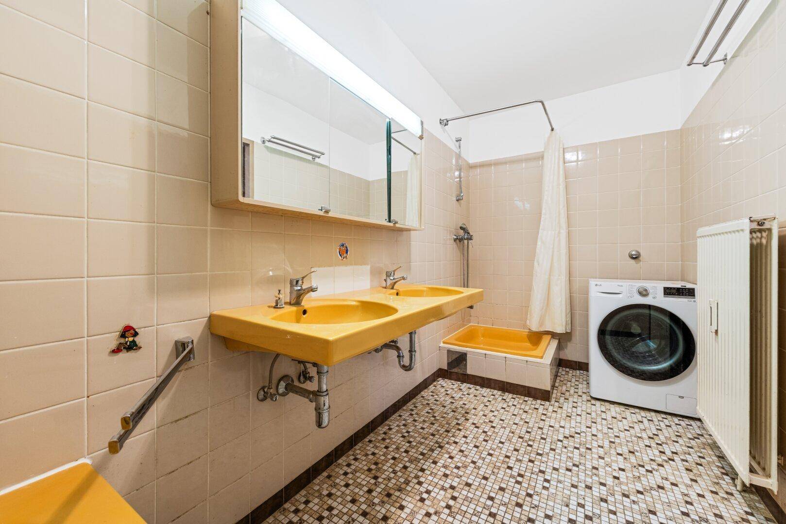 Badezimmer im Stil der 80er Jahre mit gelben Fliesen, Doppelwaschbecken und Duschbereich.