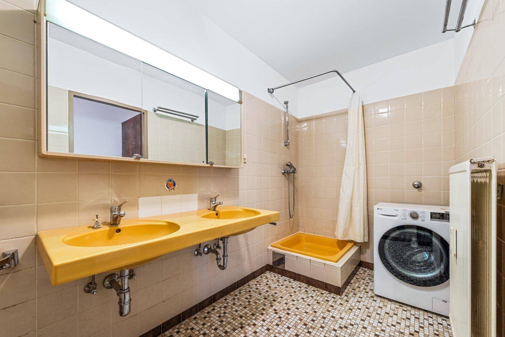 Retro-Badezimmer mit gelben Fliesen, Doppelwaschbecken und Duschbereich, inklusive Waschmaschine.