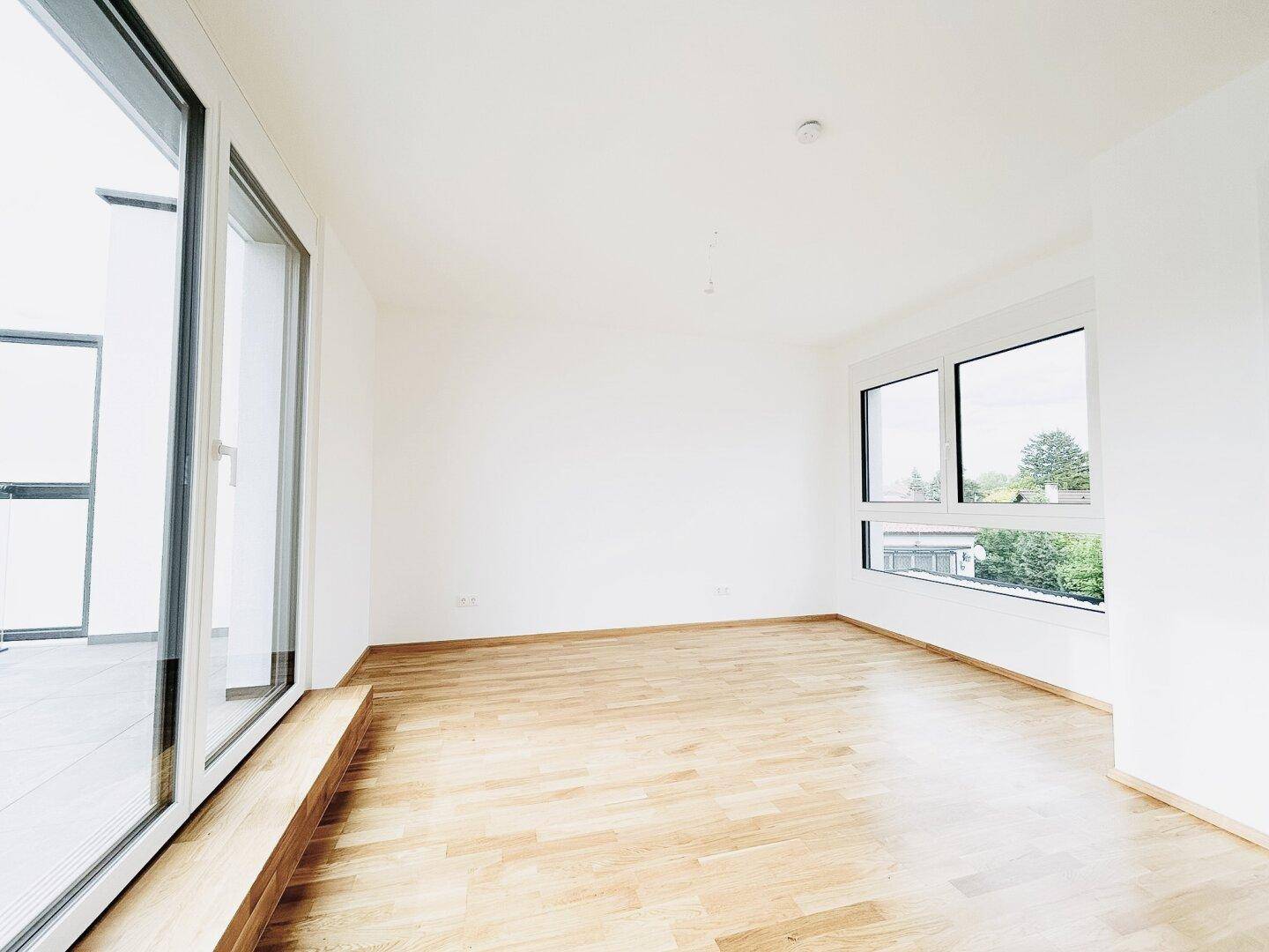 Helles, leeres Zimmer mit großen Fenstern und hellem Parkettboden, ideal für einen Wohnbereich.
