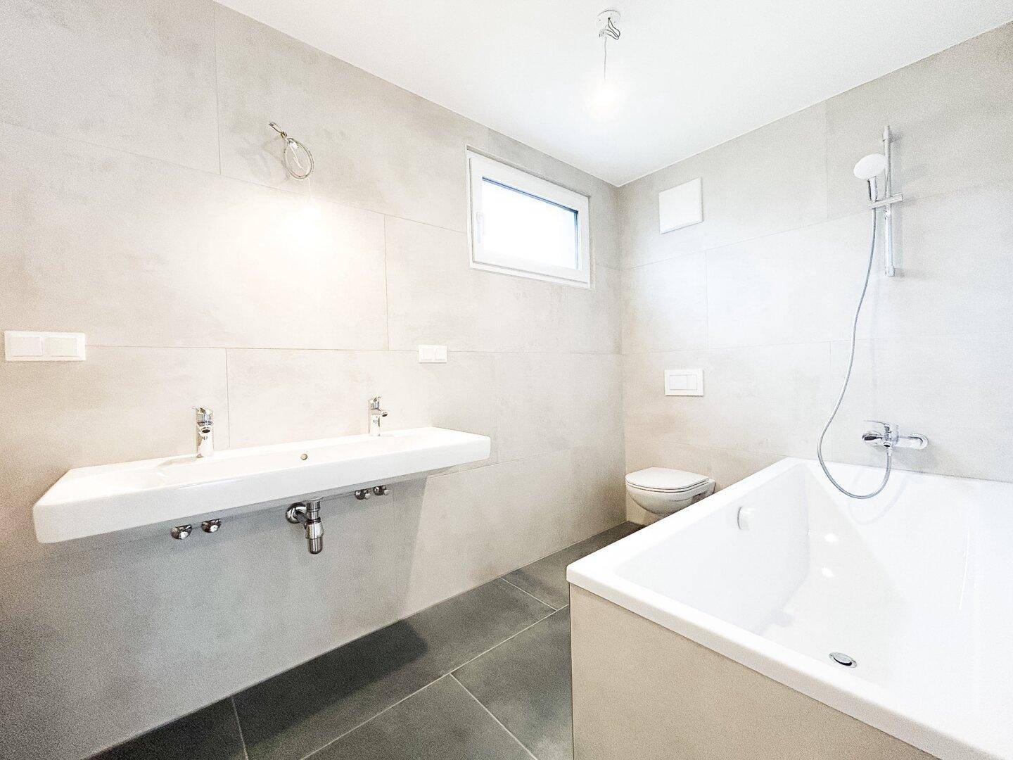 Modernes Badezimmer mit Doppelwaschbecken, Badewanne und hellgrauen Fliesen, sehr gepflegt.