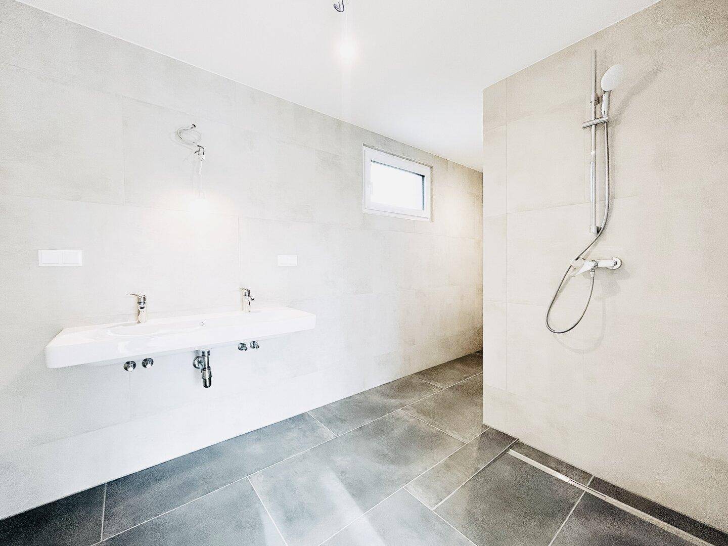 Modernes Badezimmer mit Doppelwaschbecken, ebenerdiger Dusche und hellgrauen Fliesen.
