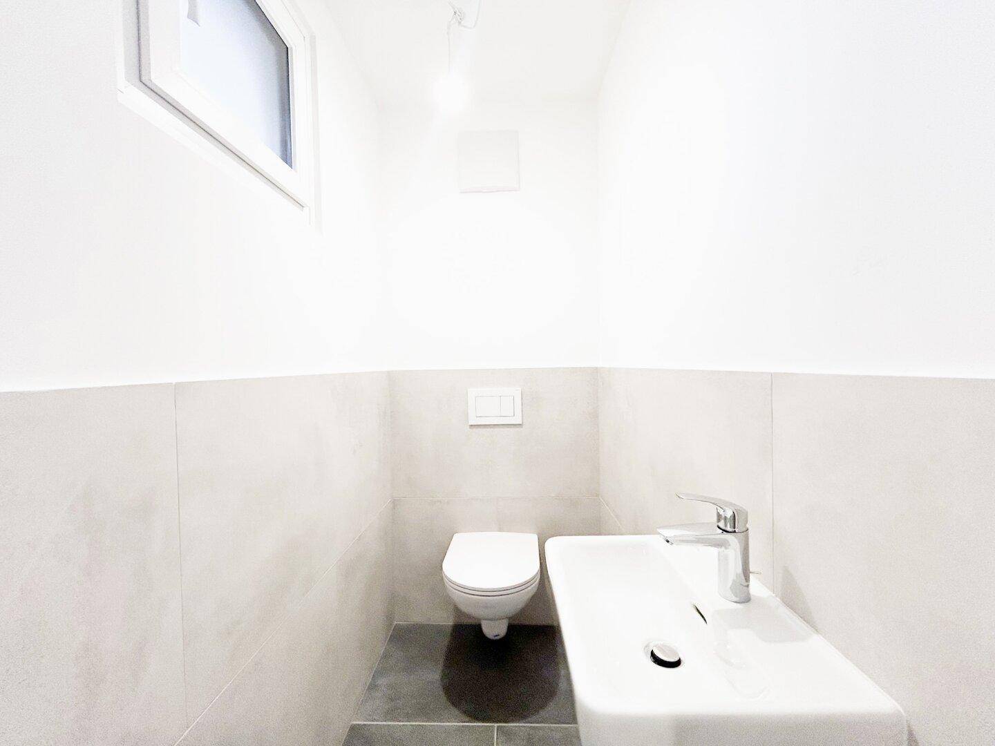 Modernes Gäste-WC mit wandhängender Toilette, Waschbecken und Fenster, sehr funktional.