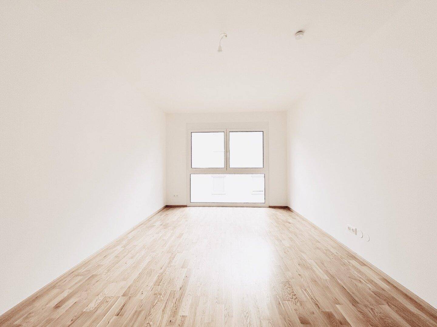Geräumiges, helles Zimmer mit Parkettboden und großem Fenster, bereit zur individuellen Einrichtung.