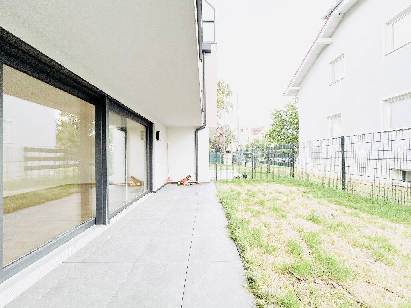 Ebenerdige Terrasse mit Fliesenboden und angrenzender kleiner Rasenfläche, ideal für den Sommer.