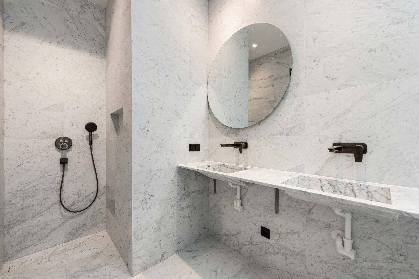 Modernes Badezimmer mit Marmorfliesen, begehbarer Dusche und Doppelwaschbecken mit schwarzen Armaturen.