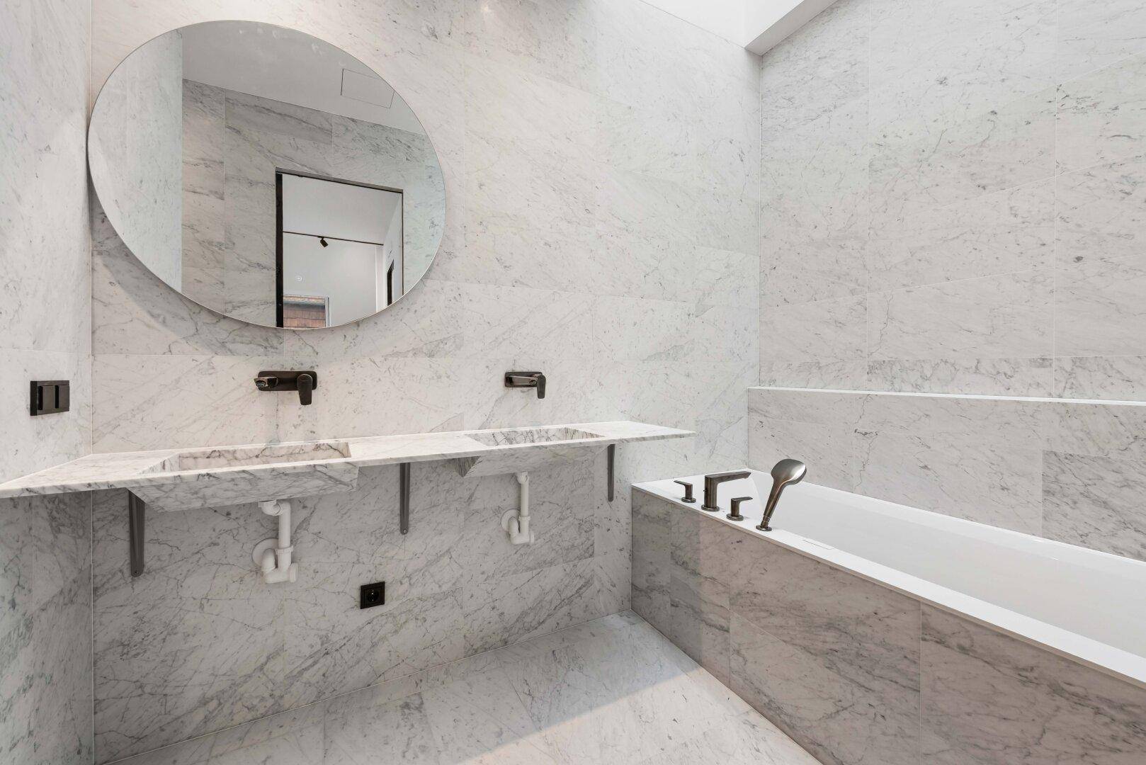 Elegantes Badezimmer mit Marmorfliesen, integrierter Badewanne und Doppelwaschbecken mit runden Spiegeln.