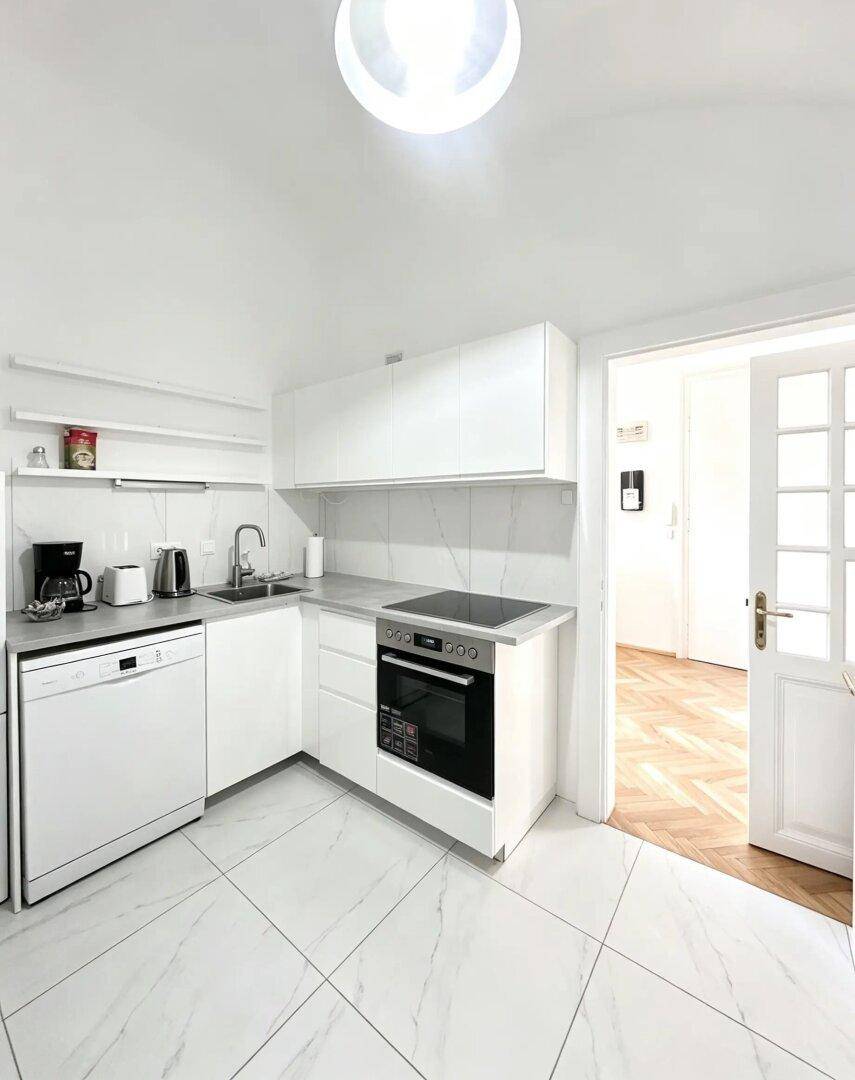 Moderne weiße Küche mit Einbaugeräten, Induktionskochfeld und großformatigen Fliesenboden.
