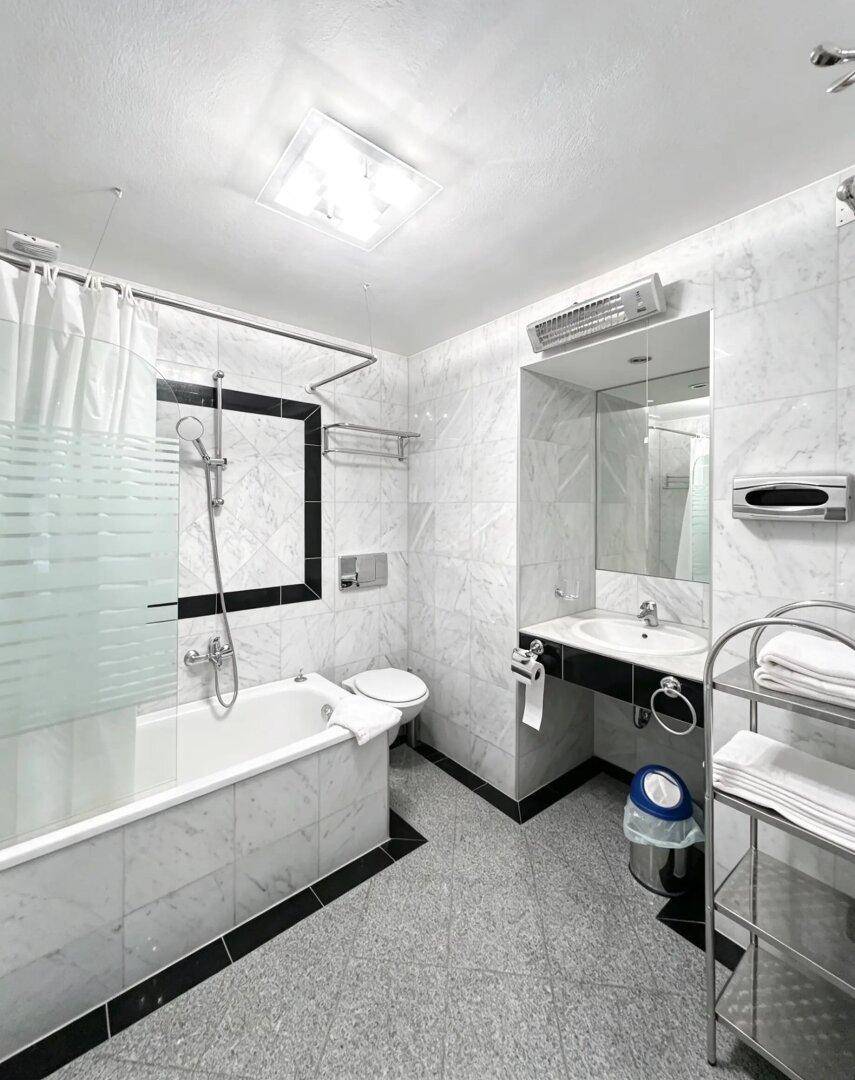Klassisches Badezimmer mit Badewanne, Dusche und Marmorfliesen an den Wänden.