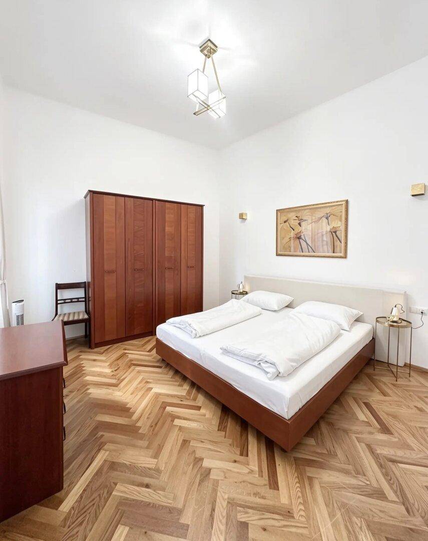 Geräumiges Schlafzimmer mit Fischgrätparkett, Doppelbett und großem Holzschrank.