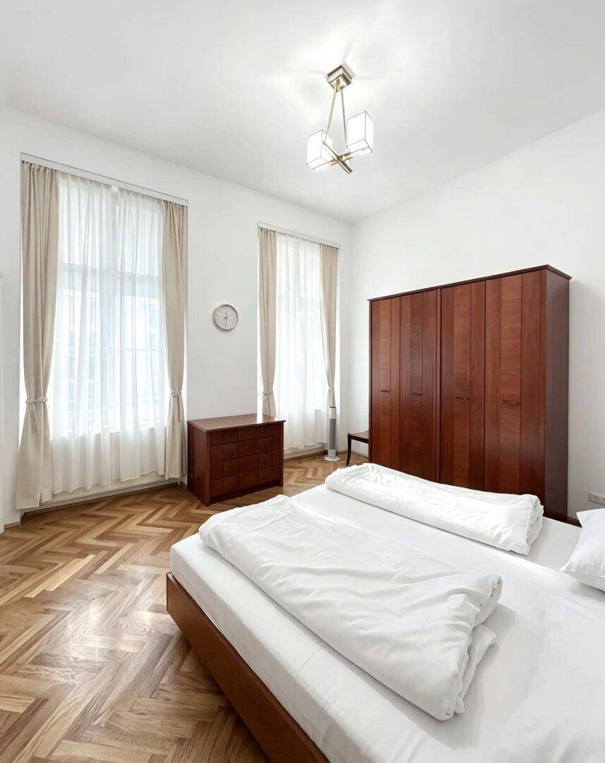 Helles Schlafzimmer mit Fischgrätparkett, Doppelbett und einem großen Kleiderschrank.