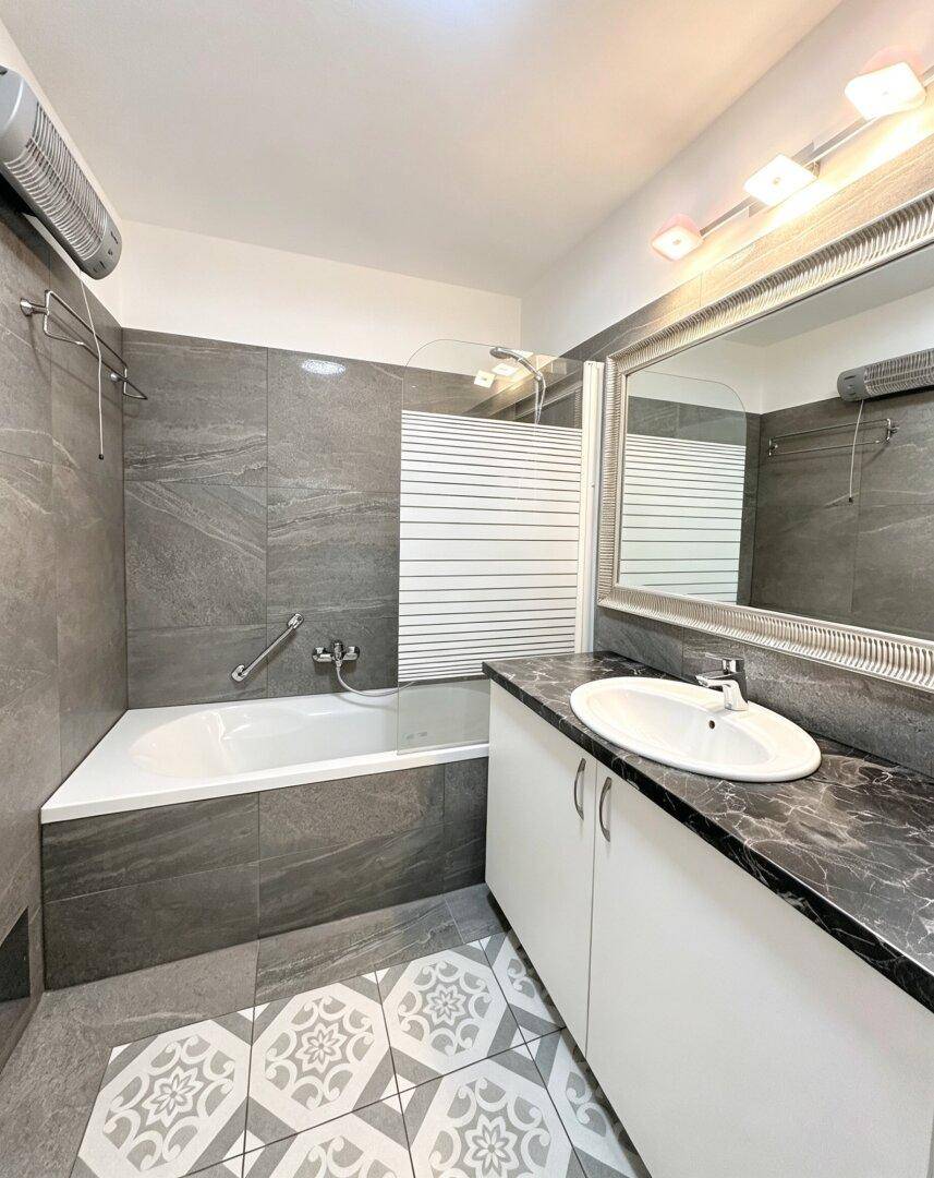 Badezimmer mit Badewanne, Waschtisch und grauen Wandfliesen.