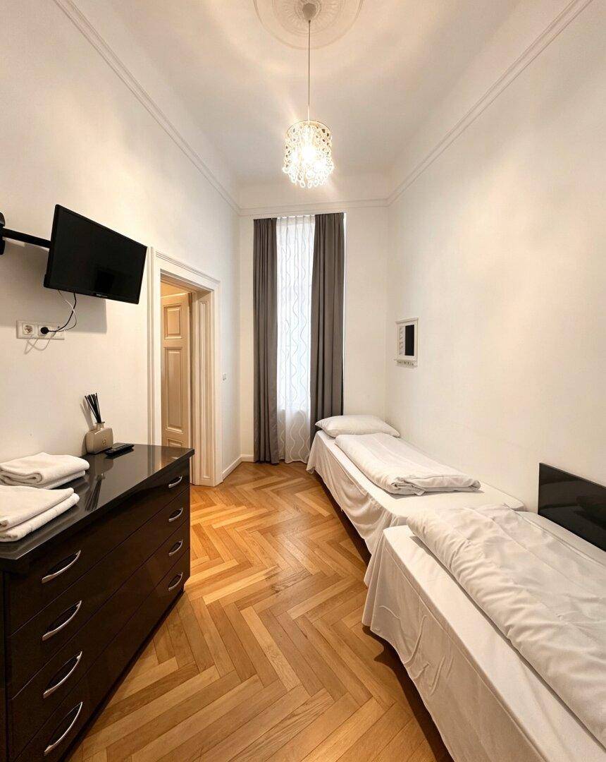 Kleines Schlafzimmer mit zwei Einzelbetten, Parkettboden und Kommode.