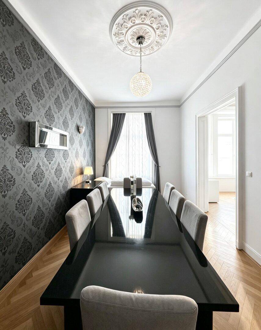 Elegantes Esszimmer mit großem Tisch, Fischgrätparkett und Stuckdecke.