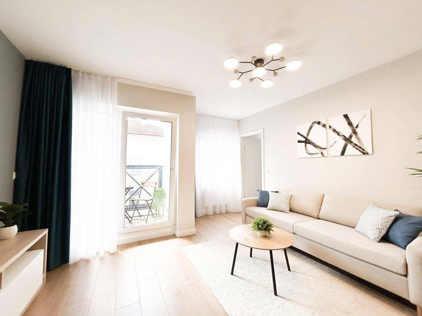 Gemütliches Wohnzimmer mit hellem Sofa, Holzboden und direktem Zugang zum Balkon.