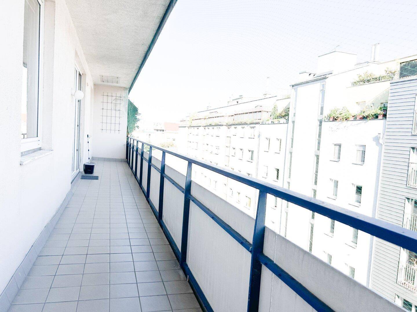 Langer Balkon mit Fliesenboden und weitem Blick über die Stadt und grüne Bereiche.