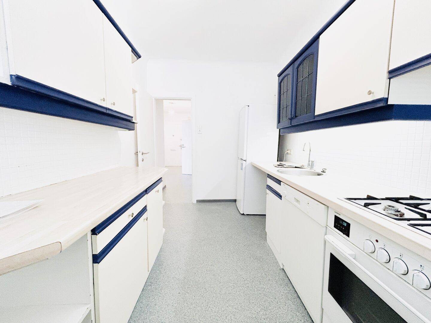 Funktionale Küche mit blauen und weißen Schränken, Herd und Kühlschrank, bereit zur Nutzung.