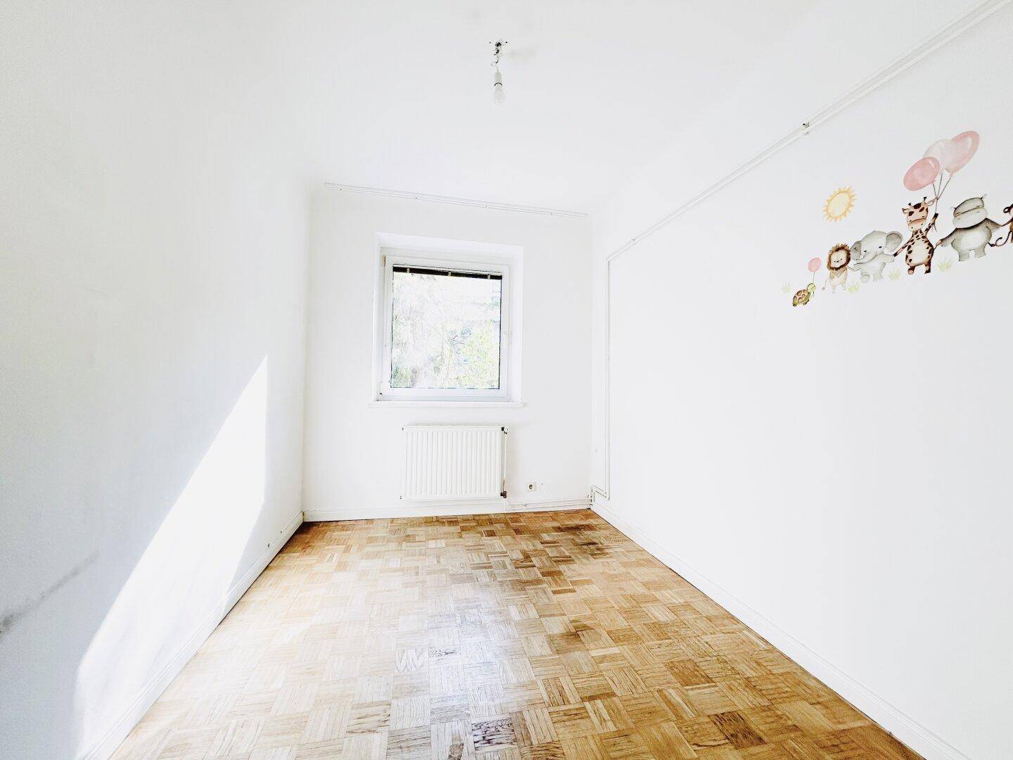 Helles Kinderzimmer mit Parkettboden, Fenster und niedlichen Wandstickern an der weißen Wand.