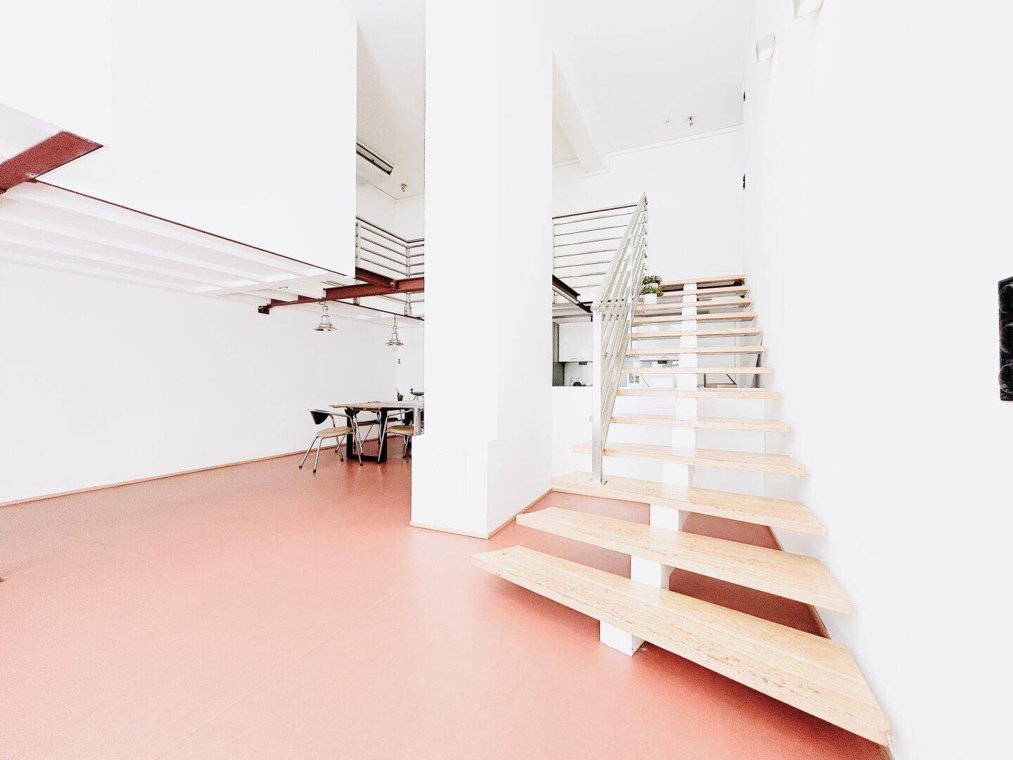 Moderne Holztreppe führt zu einem offenen Wohnbereich mit Essplatz und integrierter Küche.