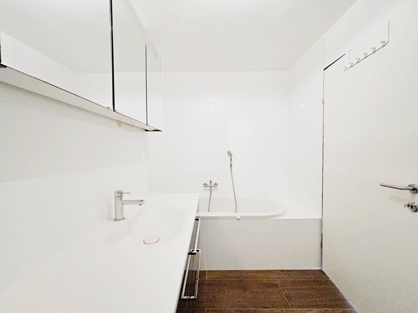 Helles Badezimmer mit Badewanne, modernem Waschtisch, Spiegelschrank und Holzboden.