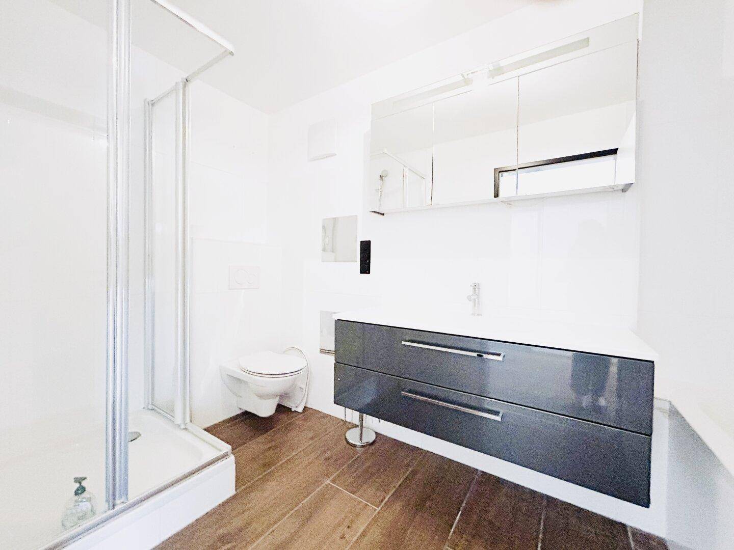 Modernes Badezimmer mit Duschkabine, dunklem Waschtisch, Spiegelschrank und wandhängendem WC.