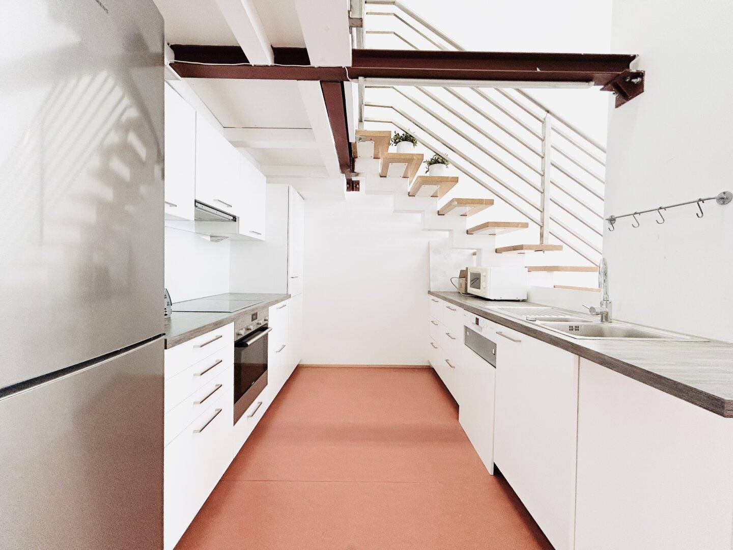 Moderne Einbauküche mit weißen Schränken und Geräten unter einer offenen Treppe.