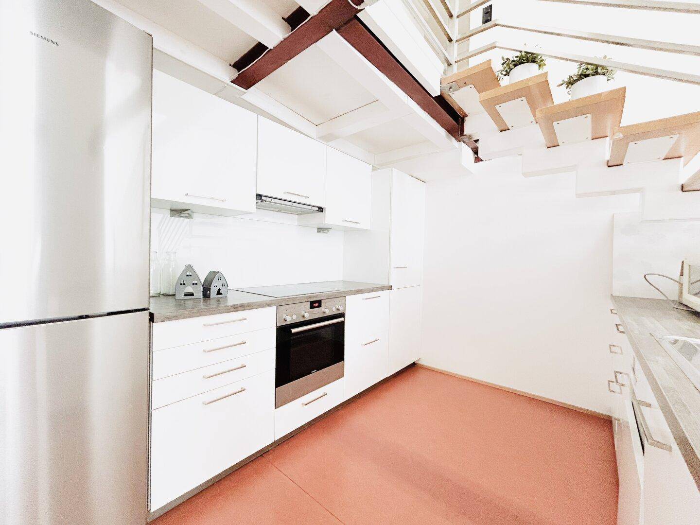 Moderne Einbauküche mit Siemens-Kühlschrank, Kochfeld und Dunstabzugshaube unter der Treppe.