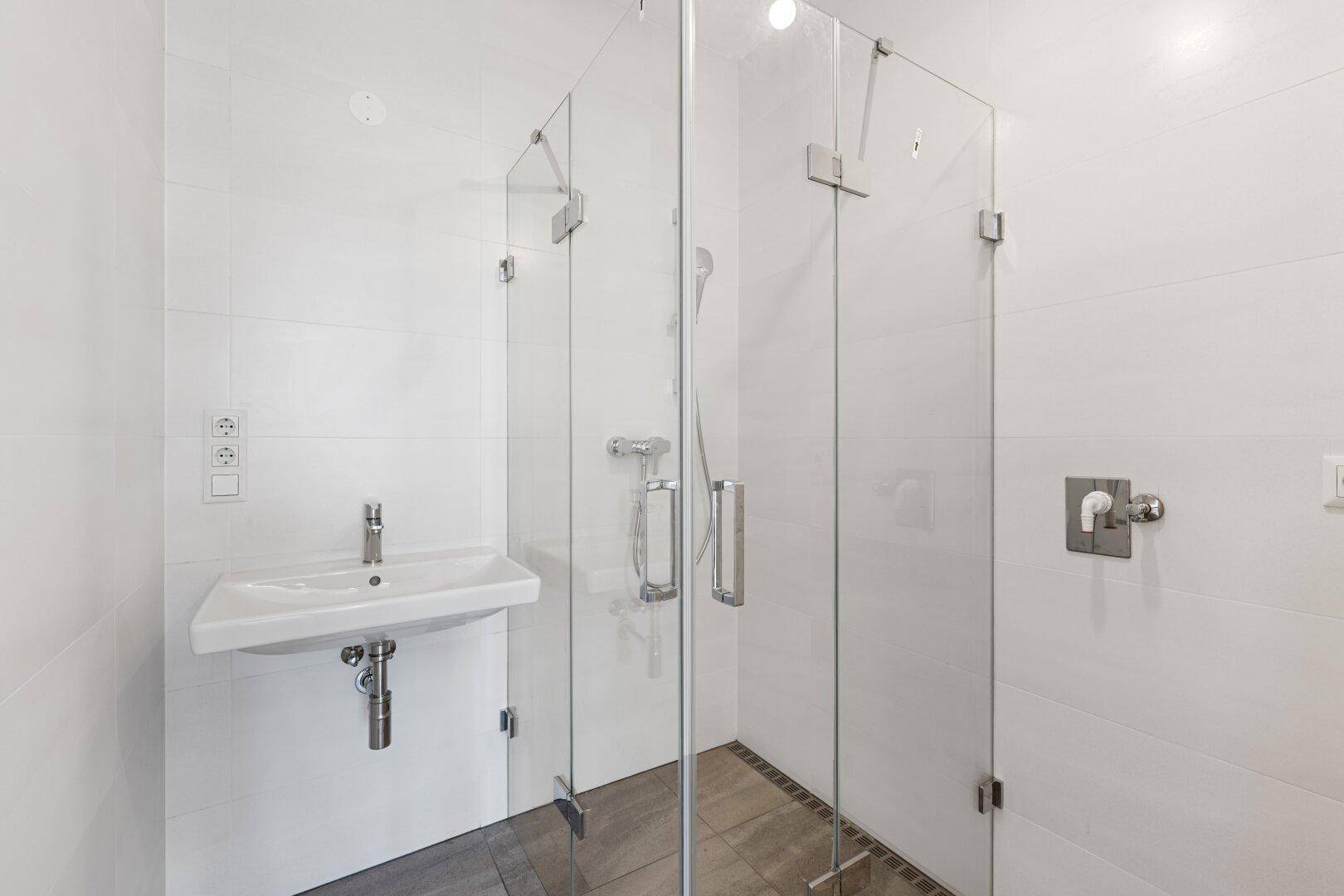Modernes Badezimmer mit weiß gefliesten Wänden, Glasdusche und Einzelwaschbecken.