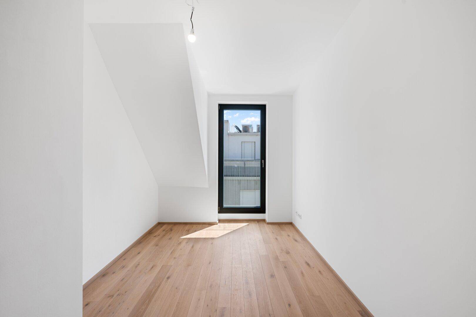 Helles Zimmer mit Holzboden und Zugang zu einem französischen Balkon.