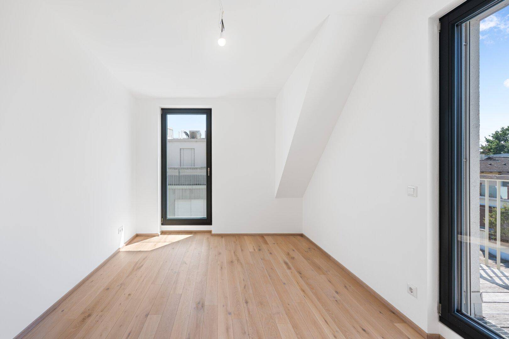 Lichtdurchflutetes Zimmer mit Holzboden und Zugang zu einem französischen Balkon.