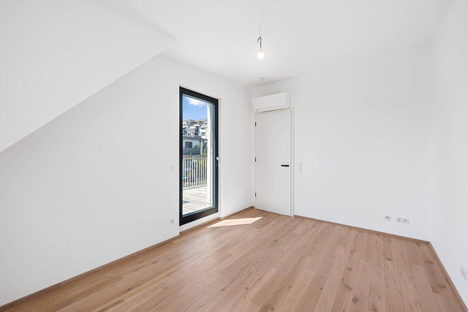 Helles Zimmer mit Holzboden, Klimaanlage und Zugang zu einem französischen Balkon.