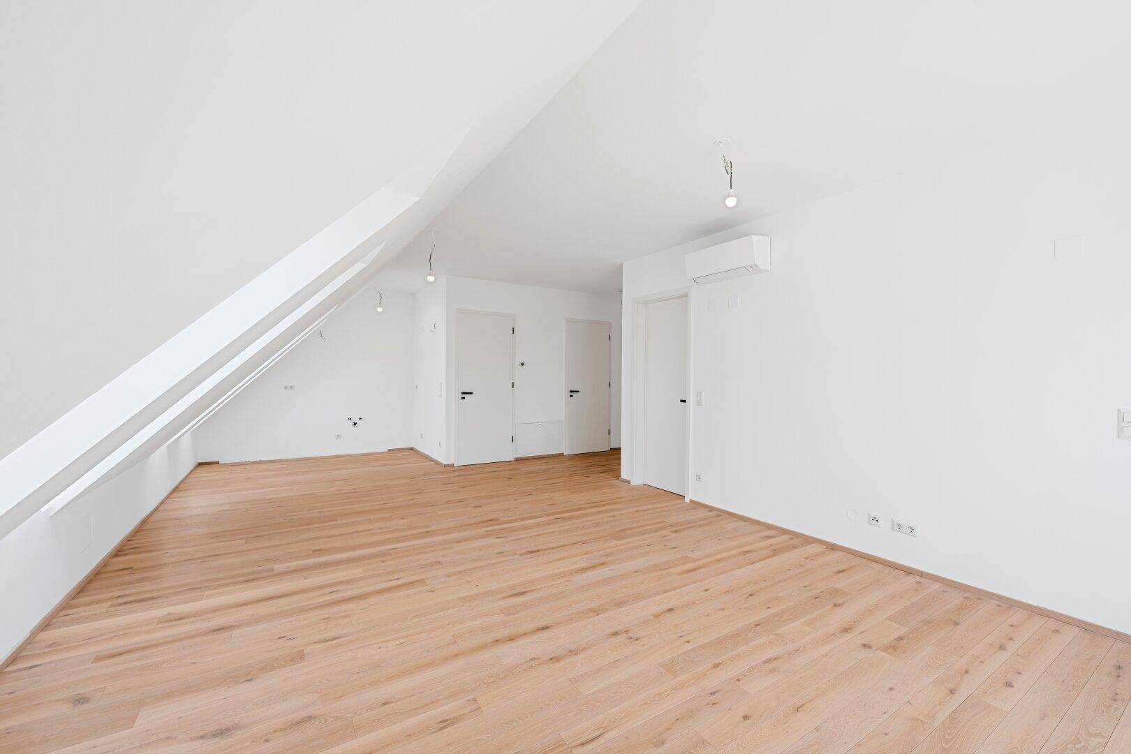 Heller, leerer Raum mit Holzboden, Dachschrägen und mehreren Türen.
