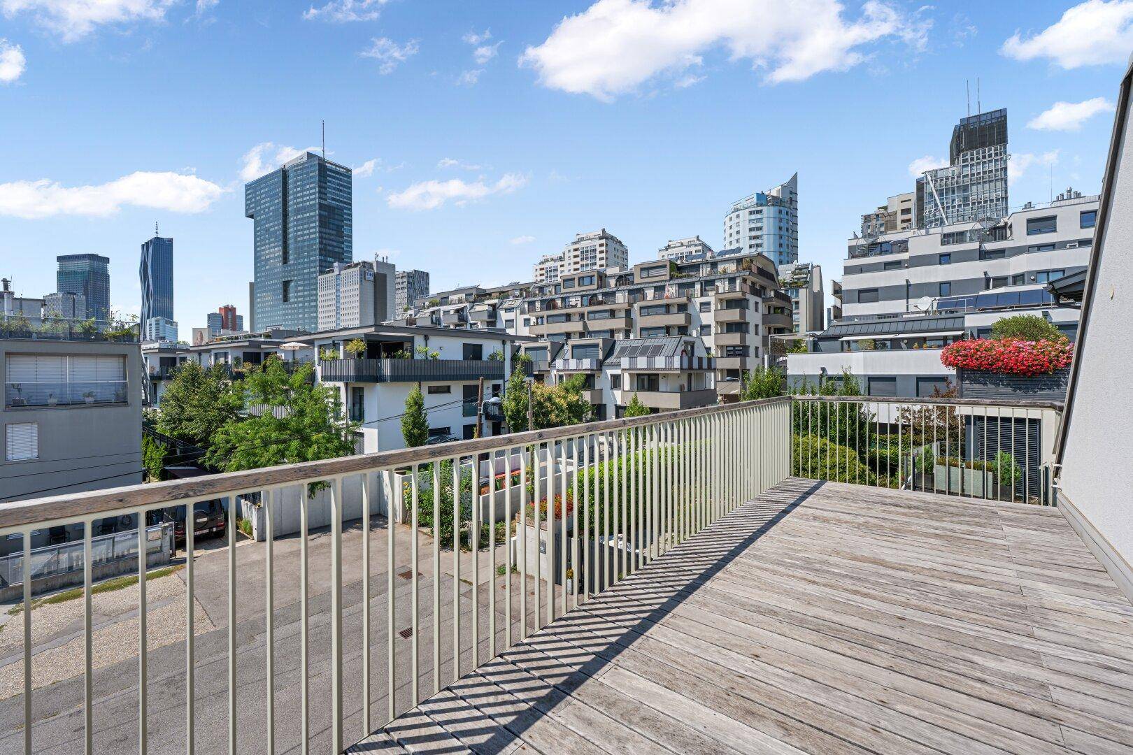 Großer Balkon mit Holzboden und weitem Blick auf die moderne Stadtarchitektur.
