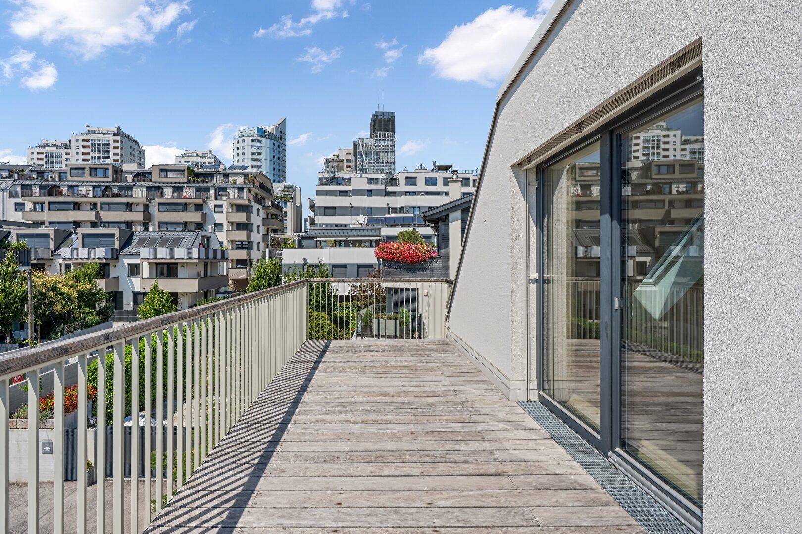 Geräumiger Balkon mit Holzboden und weitem Blick auf die moderne Stadtarchitektur.