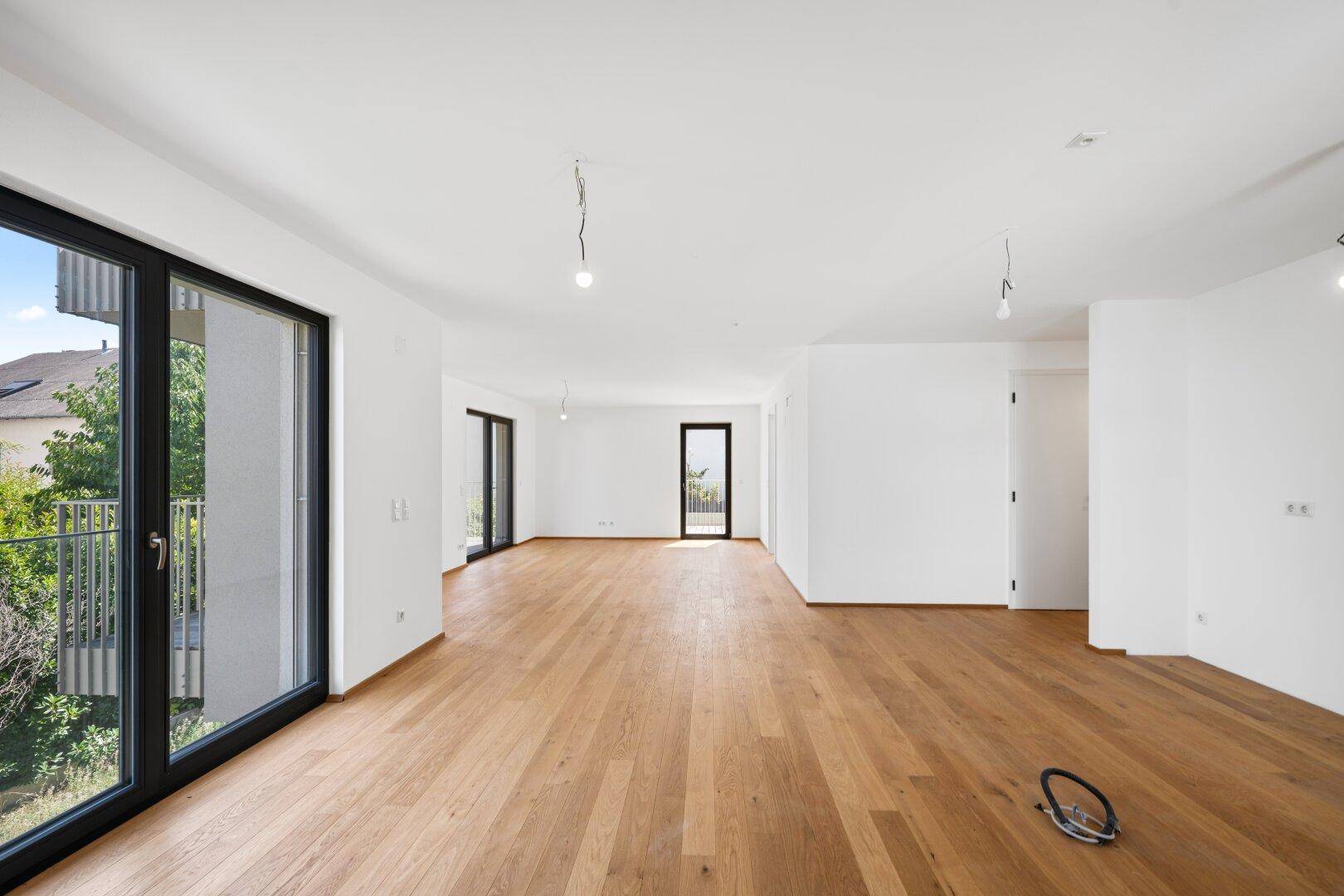 Großzügiges, helles Wohnzimmer mit Eichenparkett und mehreren Fenstertüren, die viel Licht hereinlassen.