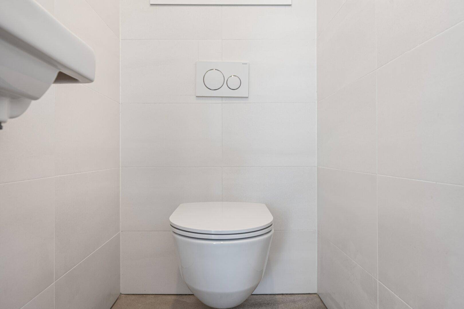 Modernes separates WC mit wandhängender Toilette und weißen Fliesen.