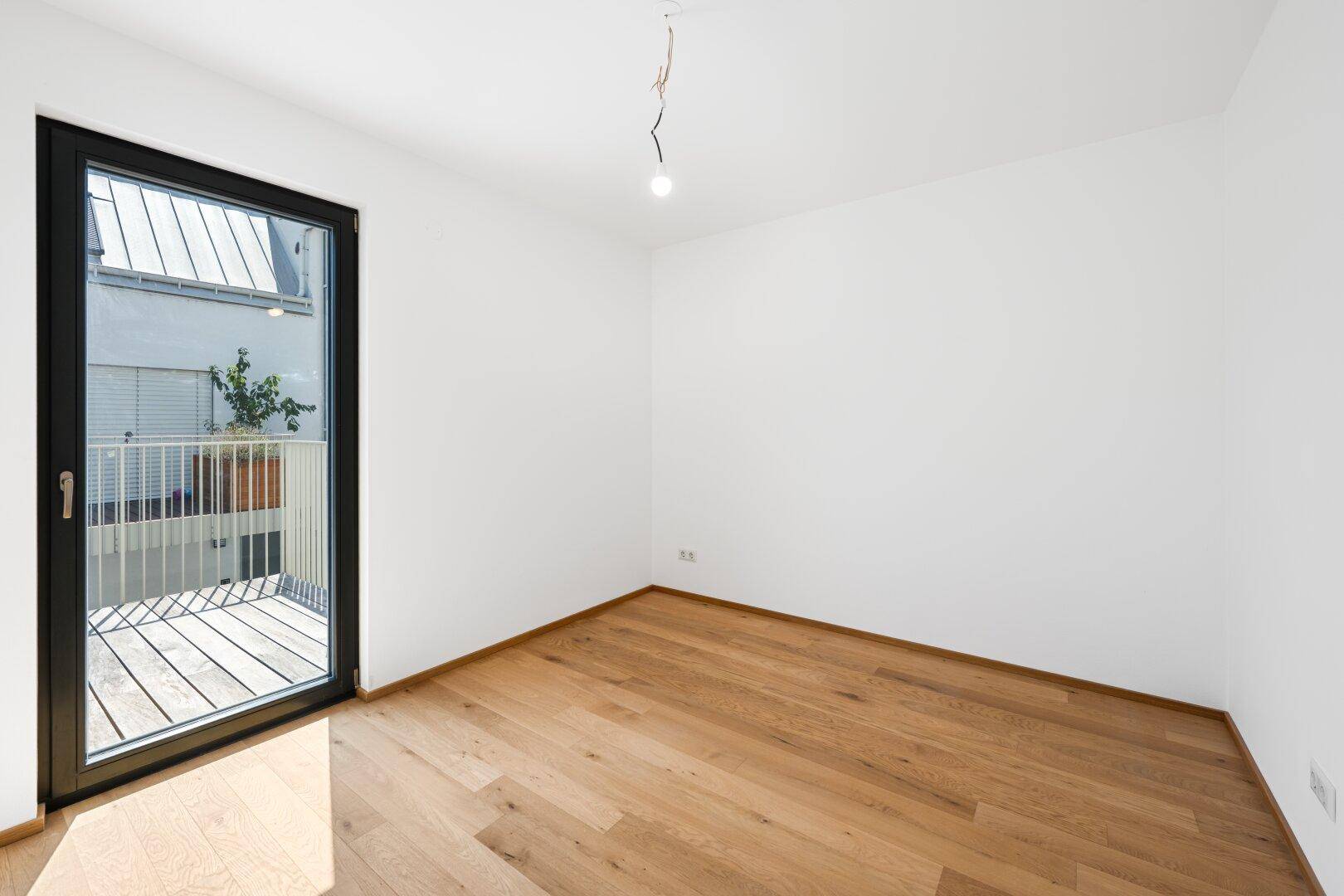 Helles Schlafzimmer mit Eichenparkettboden und Fenstertür, die auf einen kleinen Balkon führt.