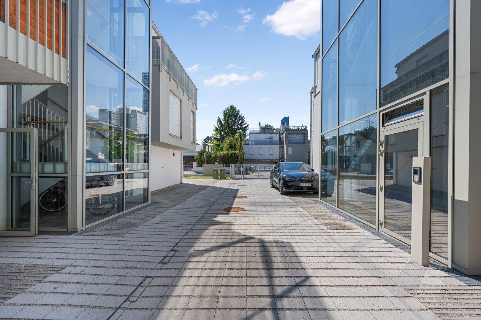 Moderner Eingangsbereich mit Glasfassade und gepflastertem Vorplatz.